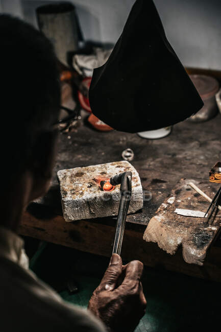 De cima cortado irreconhecível de homem étnico maduro com queima de tocha de aquecimento pedaço de metal trabalhando na mesa em oficina de artesanato — Fotografia de Stock