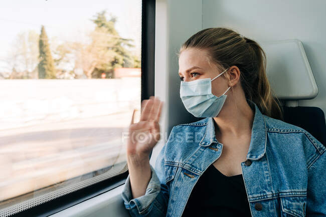 Молода жінка носить медичну маску і вітає друга на вокзалі під час їзди в поїзді і посміхається — стокове фото