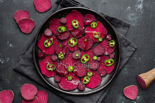 Composizione vista dall'alto di gustose fette di barbabietola preparate su teglia con peperoni verdi jalapeno e poste su asciugamano nero sul tavolo della cucina — Foto stock