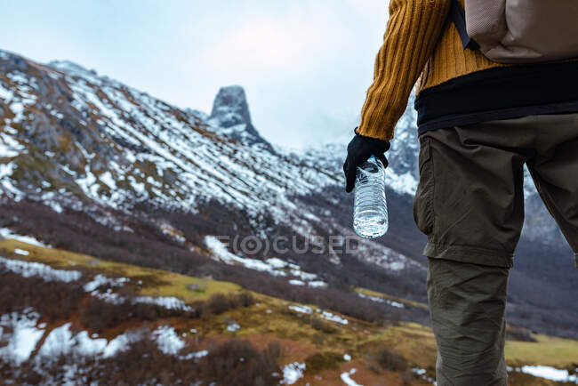 Back view anonymous tourist with backpack and in warm clothes standing on high range of Peaks of Europe and drinking water — Stock Photo