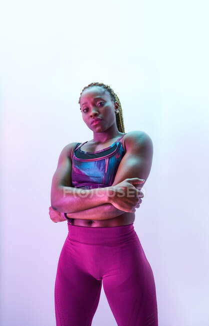 Самоуверенная афроамериканская спортсменка в спортивной одежде со сложенными руками и бицепсами, смотрящая в камеру — стоковое фото