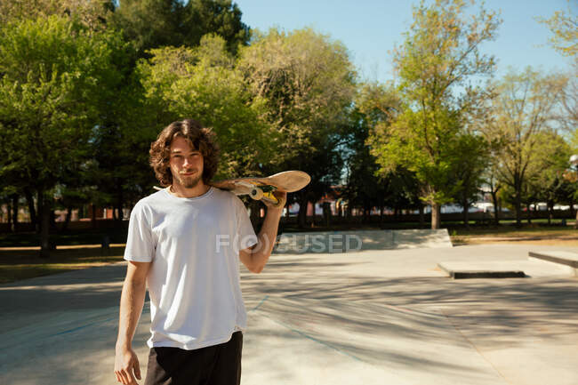 Porträt eines jungen Skateboarders, der sein Skateboard über eine Schulter hält und in die Kamera blickt. — Stockfoto