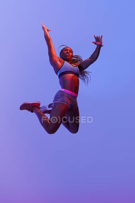 Vue latérale d'une sportive afro-américaine déterminée sautant avec des cheveux volants tout en regardant vers l'avant pendant l'entraînement cardio — Photo de stock