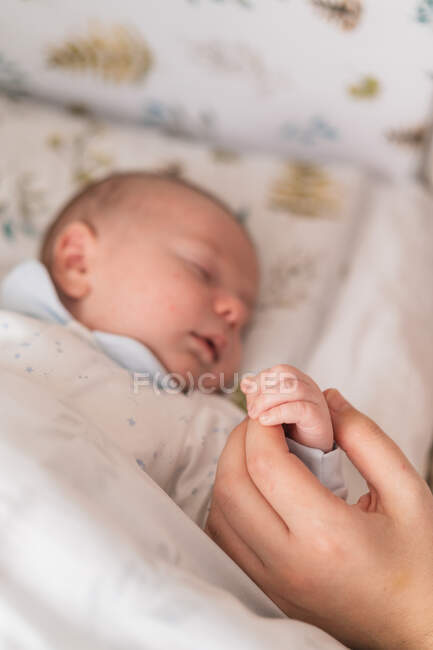 Schnupfen anonymer Elternteil mit niedlichen schlafenden Neugeborenen hält Hände zu Hause auf verschwommenem Hintergrund — Stockfoto