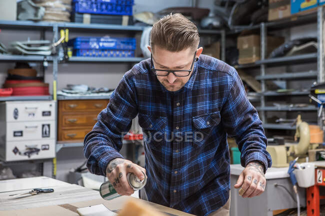 Concentrated male artisan applying aerosol paint on piece of fabric while creating upholstery for motorcycle seat at workbench — Stock Photo