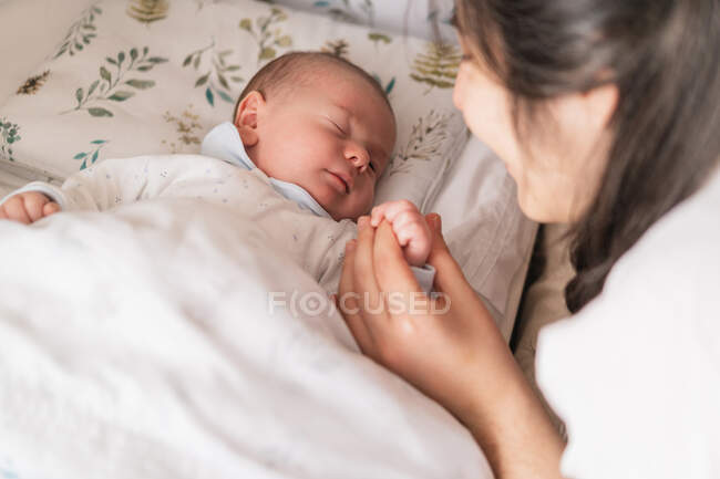 Ritaglia genitore anonimo con carino sonno neonato tenendosi per mano a casa su sfondo sfocato — Foto stock