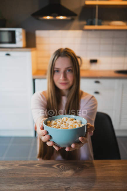Jovem fêmea olhando para a câmera com tigela redonda em forma cheia de deliciosos anéis de milho no leite para o café da manhã em casa — Fotografia de Stock