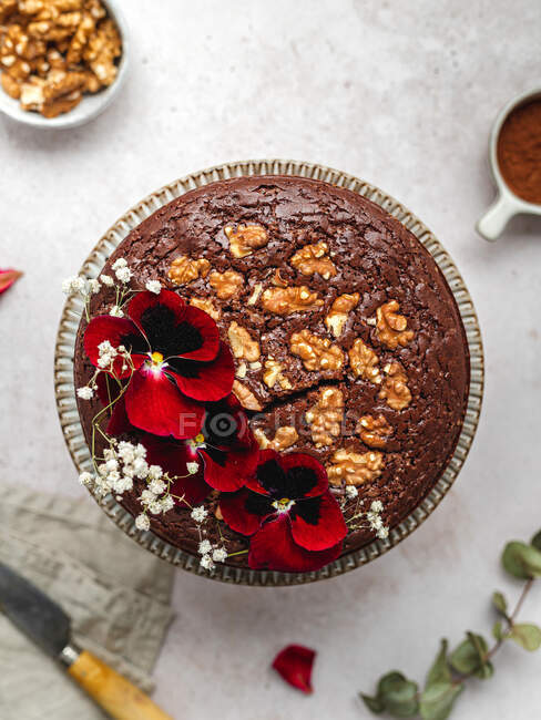 Зверху солодкий шоколадний торт, прикрашений червоними квітами та волоськими горіхами, що подаються на столі — стокове фото