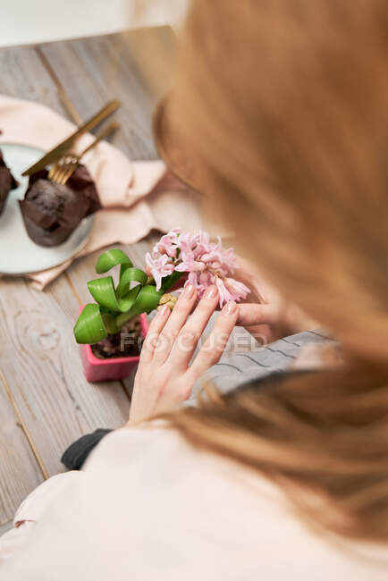 Alto ângulo de cultura fêmea anônima com flor florescente raminho acima da mesa com sobremesa assada durante o processo de cozimento em casa — Fotografia de Stock