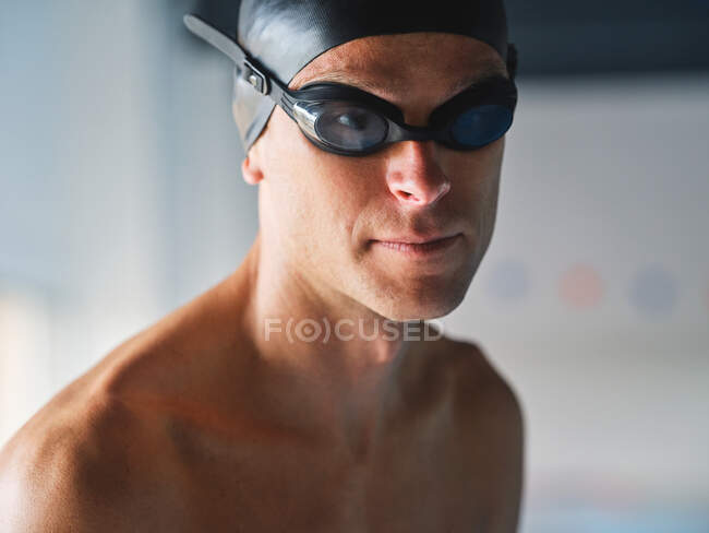 Маскулінний чоловічий плавець у професійних окулярах з м'язовим тілом, що стоїть перед тренуванням на сонячному світлі на розмитому фоні, дивлячись на камеру — стокове фото