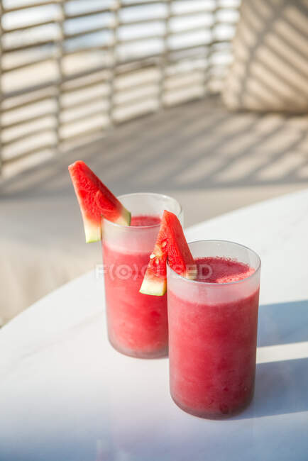 High angle pair of glasses of fresh squeezed watermelon smoothie served on table near soft comfy sofa on grassy lawn in garden — Fotografia de Stock