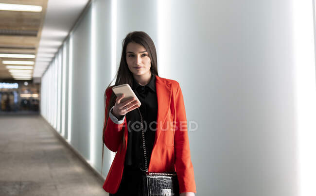 Contenuto femminile in abito alla moda in piedi nel corridoio del moderno centro commerciale e smartphone di navigazione — Foto stock