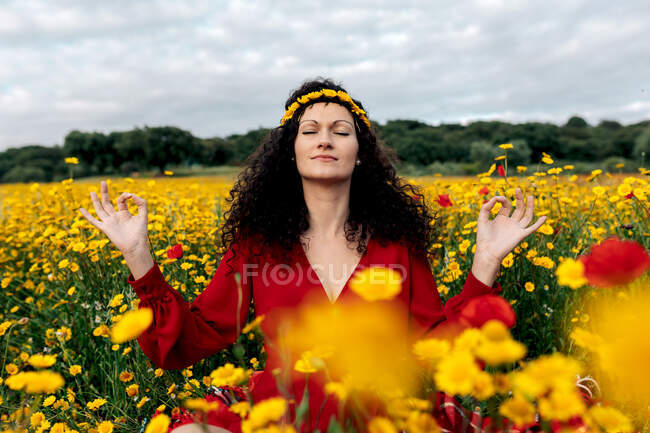 Donna concentrata in corona di fiori praticare yoga con gli occhi chiusi tra margherite in fiore e Papaver sul prato in campagna — Foto stock