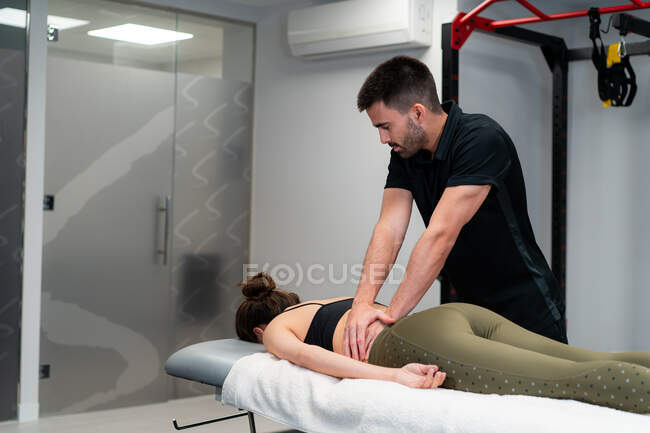 Небритый физиотерапевт-мужчина массирует спину анонимной женщины в постели во время медицинской процедуры в больнице — стоковое фото