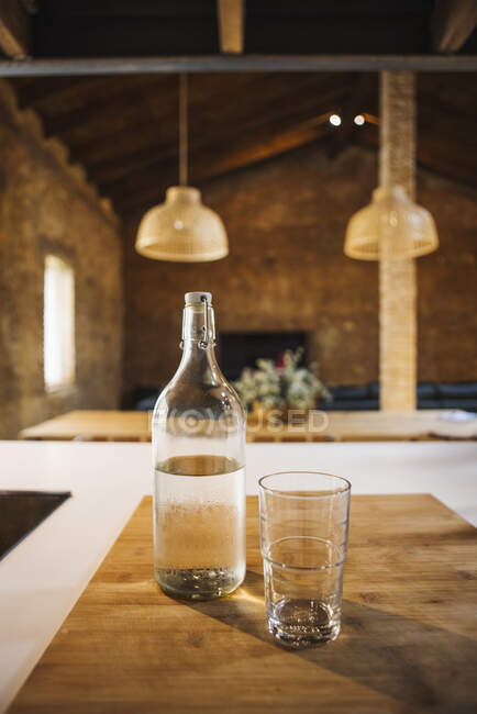 Прозрачная бутылка и стекло из чистого аква на деревянной доске с тенью на кухне — стоковое фото
