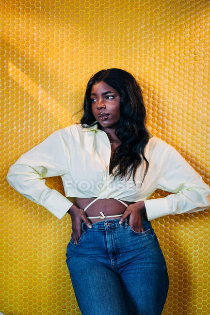 Selbstbewusste Afroamerikanerin im trendigen Outfit steht auf leuchtend gelbem Hintergrund und schaut weg — Stockfoto