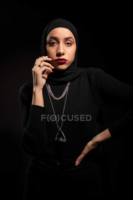 Jovem mulher islâmica atraente vestindo roupa preta e hijab tocando o rosto suavemente e olhando para a câmera — Fotografia de Stock