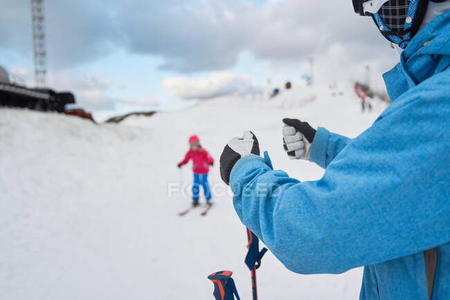 Pais sem rosto em roupas esportivas quentes ensinando a criança a esquiar ao lado de encostas nevadas na estância de esqui de inverno — Fotografia de Stock