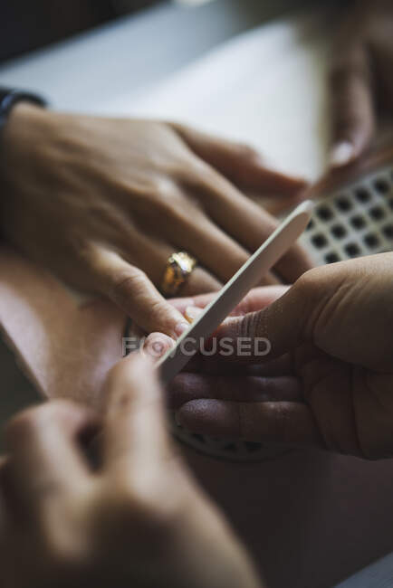From above of crop faceless manicurist filing nails of unrecognizable client with file during procedure in beauty salon — Stock Photo