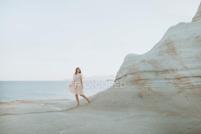 Femme en robe blanche se promenant le long d'un étroit passage formé par de légers rochers courbés par temps ensoleillé à Sarakiniko Grèce — Photo de stock