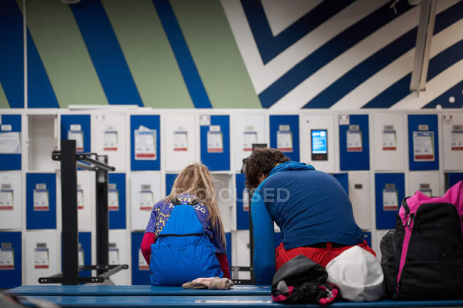 Vista posteriore di padre e figlia anonimi seduti sulla panchina nello spogliatoio e che indossano l'attrezzatura per lo sci — Foto stock