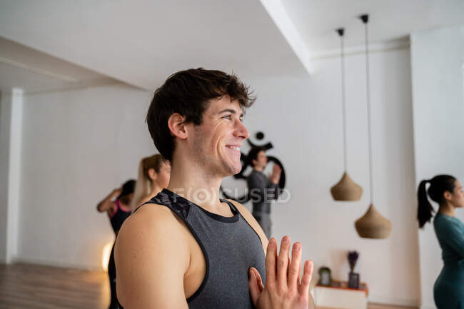 Vue latérale d'un homme joyeux en tenue de sport debout en montagne avec des mains de prière posant et faisant du yoga pendant les cours en studio — Photo de stock