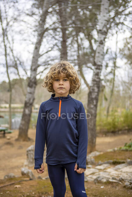 Очаровательный ребенок в спортивной одежде носить смотреть в камеру на размытом фоне при дневном свете на открытом воздухе — стоковое фото
