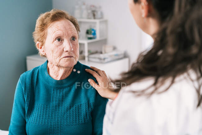 Crop anonymous doctor speaking with scared sad elderly woman while looking at each other during examination in hospital — Stock Photo