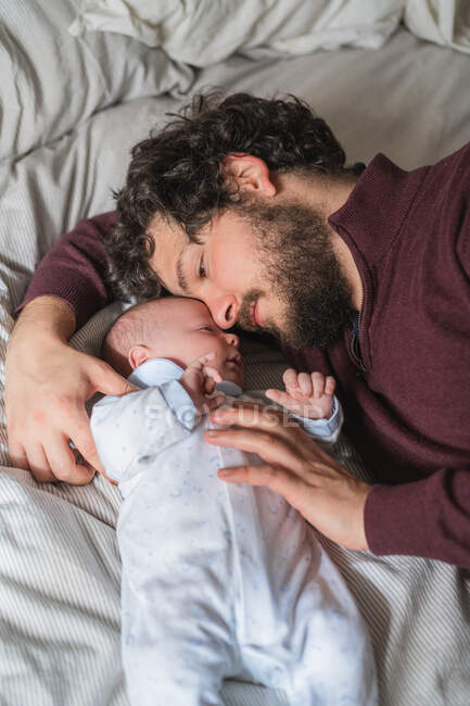 High angle of bearded dad embracing cute little child while lying on creased bed and looking at each other — Stock Photo