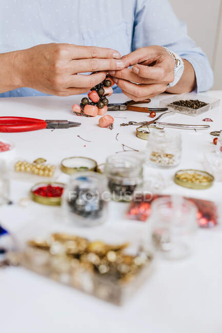 Side view of crop anonymous female master with instrument making necklace at table with different tools — Stock Photo