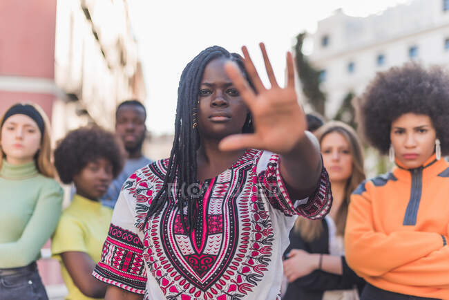 African American female standing on street in crowd of diverse people and showing stop sign while looking at camera during Black Lives Matter demonstration — Stock Photo
