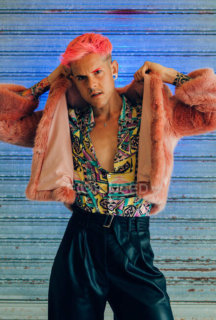 Jovem homossexual homem na moda desgaste com manicure e corte de cabelo moderno olhando para a câmera no fundo azul — Fotografia de Stock