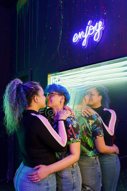 Giovani sorridenti fidanzate omosessuali che si abbracciano guardando l'un l'altro e riflettendo nello specchio sotto Godere di iscrizione — Foto stock