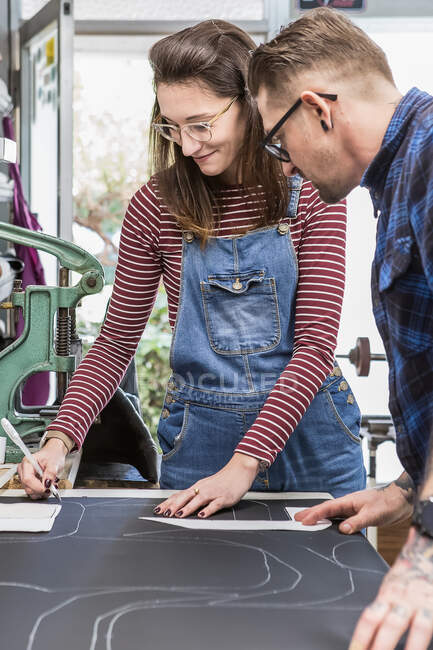 Couple of creative artisans marking piece of black leather while creating upholstery for motorcycle seats in workshop together — Stock Photo