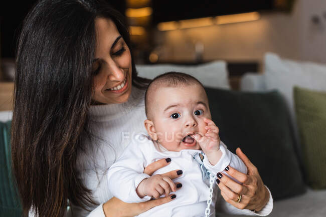 Восхищенная мать держит восхитительно улыбающегося малыша и веселится вместе дома — стоковое фото