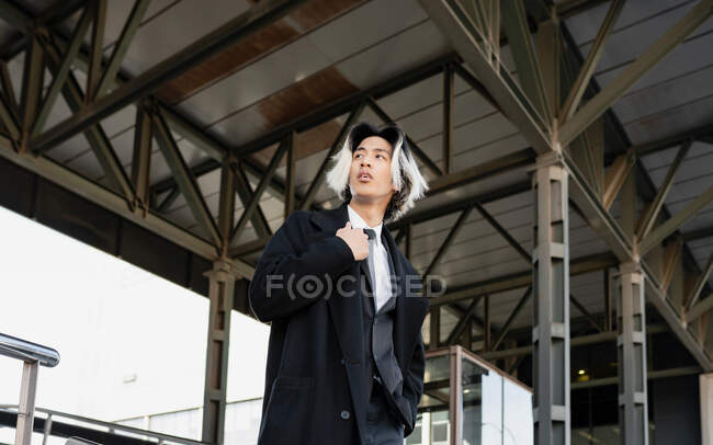 Знизу молодого добре вдягненого азіатського чоловіка з пофарбованим волоссям, що оглядається в місті. — стокове фото