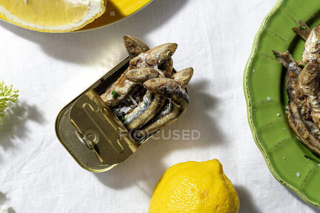 From above of fried and canned anchovies served on table with fresh lemons in restaurant in sunlight — Foto stock