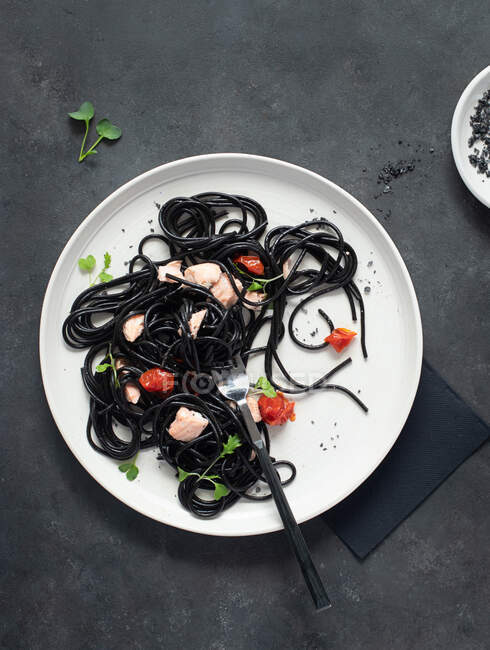 Spaghettis à l'encre noire avec saumon dans une assiette en céramique sur fond sombre — Photo de stock