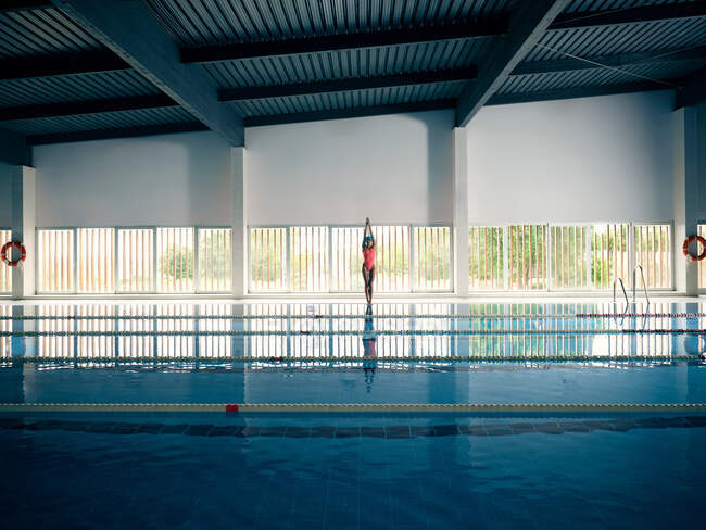 Atleta anonima in costume da bagno in piedi a bordo piscina contro l'acqua pura con corsie durante l'allenamento in edificio moderno — Foto stock