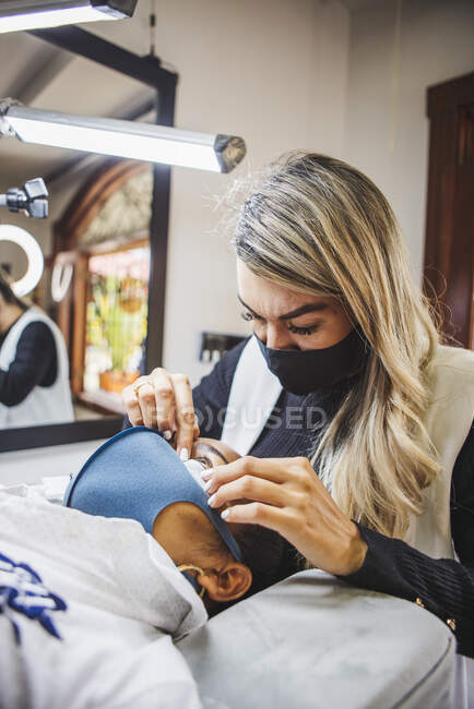 Косметолог нанесла пластырь на лицо этнического клиента в маске для лица в салоне — стоковое фото