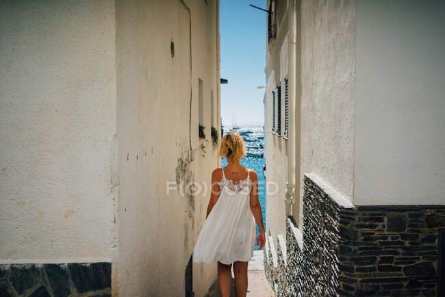 Вид ззаду на анонімну безтурботну жінку-туристку, що йде по вузькій вулиці між старими будівлями міста — стокове фото