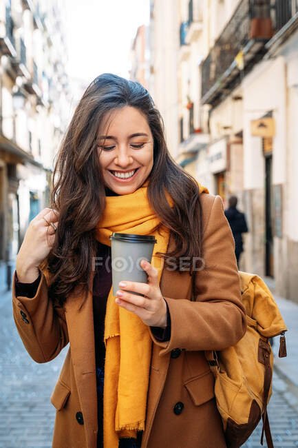 Front view of laughing female with hot drink on city street — Stock Photo