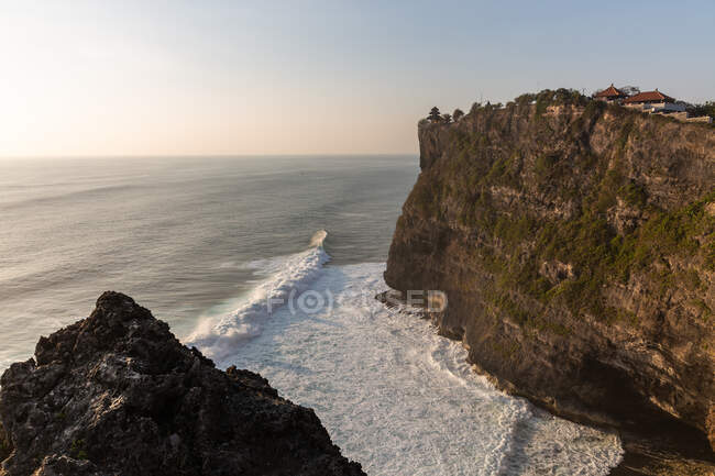 Rough rocky cliff washed by wavy foamy sea under cloudless blue sky in scenic nature — Stock Photo