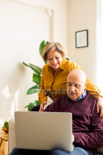 Веселая зрелая пара разговаривает в видеочате на ноутбуке в гостиной — стоковое фото
