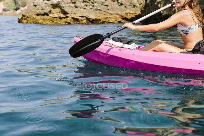 Vue latérale d'un voyageur méconnaissable avec des pagaies flottant sur de l'eau de mer turquoise près du rivage rocheux par une journée ensoleillée à Malaga en Espagne — Photo de stock