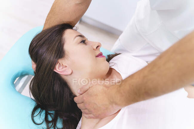 De arriba de la cosecha irreconocible fisioterapeuta masculino que revisa el cuello del paciente adulto en la cama en el hospital - foto de stock