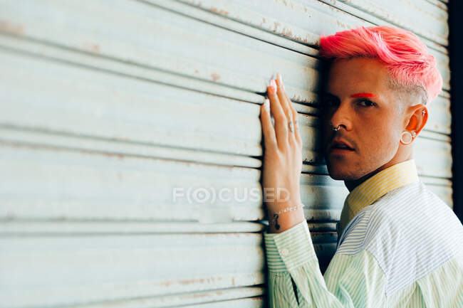 Vista laterale di giovane transgender uomo in camicia a righe con taglio di capelli moderno guardando la fotocamera su sfondo grigio — Foto stock