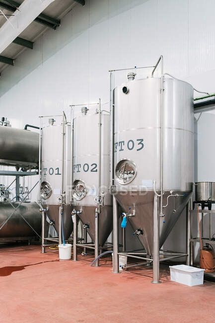 Stainless steel mash boiler near lauter tun with hoses on floor in light brewing company — Stock Photo