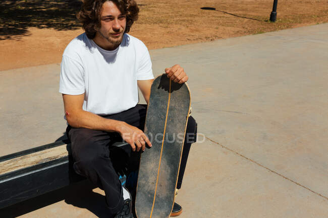 Чоловік сидить тримаючи свій скейтборд в сонячний день — стокове фото