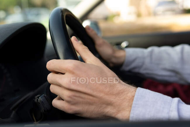 Side view of crop faceless male with hands on steering wheel driving contemporary car - foto de stock
